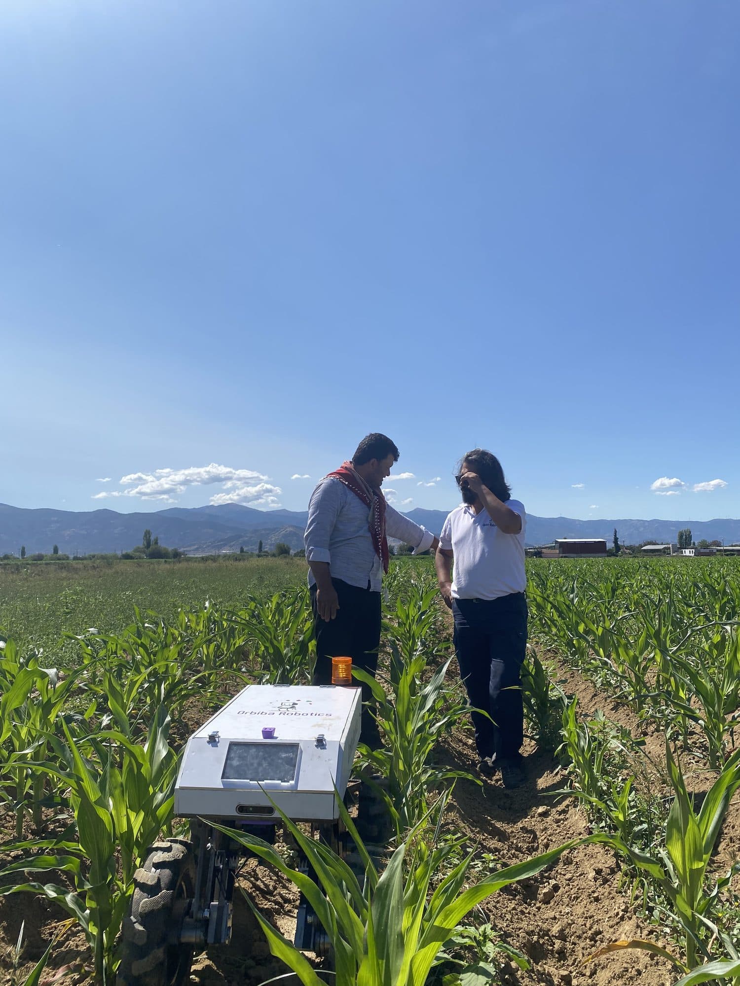 Two team members talking beside Ecominos between rows of corn