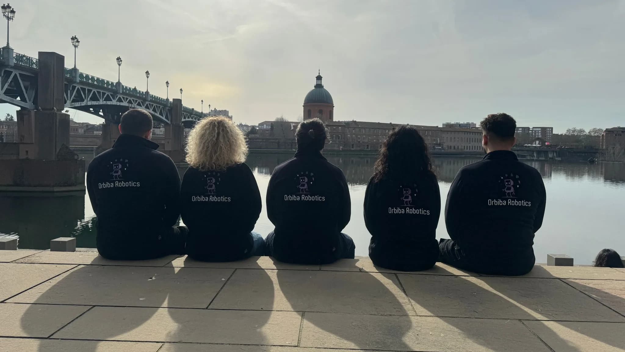 The Orbiba team sitting by the river in Toulouse in Orbiba Robotics jackets